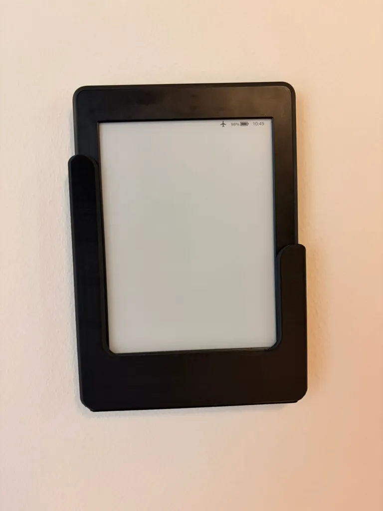 The Kindle in its black wall mount with a completely blank white screen. Only the status bar remains, showing aeroplane mode, 98% battery and 10:49.